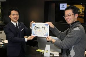 富山のグループから贈られた１００回記念の額を披露する寺西さん（左）と宮崎さん＝中村区名駅４で