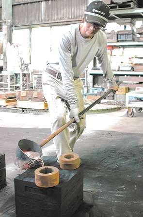 鋳型に溶けたアルミニウムを注ぐ新実善明さん＝西尾市平坂町のマル天鋳造所で
