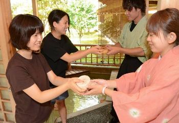 ホテルで就業体験するインターン仲間に尾鷲ヒノキの板を手渡す（左から）山田さん、竹ノ谷さん＝紀北町紀伊長島区東長島のホテル季の座で