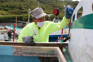 水漏れの場所を探し当て、グラスファイバーを塗る飯島誉富さん＝千葉県旭市の飯岡漁港で
