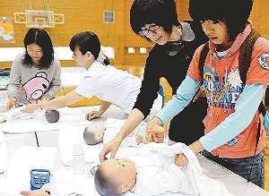 新生児を模した人形を使い、おむつ交換に挑戦する児童＝津市の県立看護大で