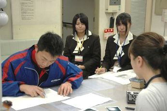女性社員（右）の窓口業務を真剣な表情で観察する生徒たち（中央の２人）＝四日市市北条町の中部電力四日市営業所で