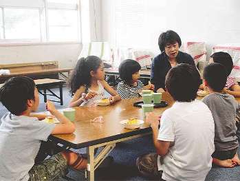 午後５時、子ども指導員とおやつを食べる小学生たち＝名古屋市の広路小学校で