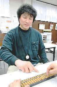 生徒の席を回り、そろばんの玉の動かし方を見せて指導する関谷樹弘さん＝岐阜県笠松町で