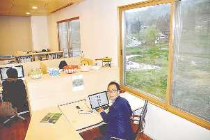 雑誌「自遊人」の編集部で仕事をする岩佐十良さん（手前）。窓越しには、四季折々の自然が＝いずれも新潟県南魚沼市で