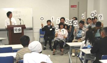会場からの質問に札を挙げて回答するパネリストたち＝中区栄３の市民活動推進センターで