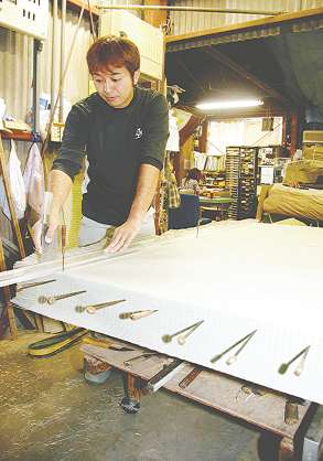 土台に合わせ包丁で畳表をまっすぐ切っていく中村勝利さん＝豊橋市佐藤の中野製畳所で