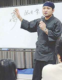「夢・ありがとう」の文字を背に講演する杉浦誠司さん＝美濃加茂市で