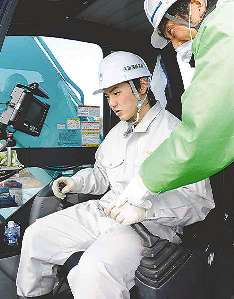 最新式のショベルカーの操作を体験する男子生徒＝津市須ケ瀬町の雲出川河川敷で