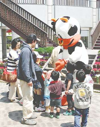 子どもたちに囲まれて握手する藤原記者が入ったモーくん＝田原市野田町のサンテパルクたはらで