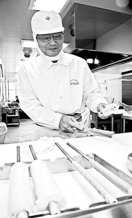 器用な手つきで出刃を使い魚のすり身を竹棒に巻き付けていく堀田正勝さん＝豊川市豊が丘町の「ちくわの里」で