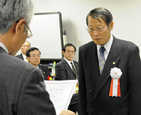 指定通知書の交付を受ける県社労士会の片境会長（右）＝県民会館で
