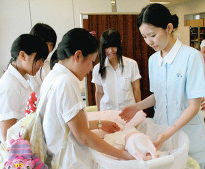 学生（右）から赤ちゃんの抱き方を学ぶ高校生ら＝津市夢が丘の県立看護大で