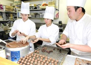 永喜多信行さん（右）の指導でトリュフチョコを作る中学生たち＝東京都江戸川区