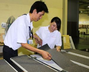 先輩社員に教わりながら幕板に防音材を取り付ける田中さん（右）＝春日井市上田楽町のキタガワ工芸で