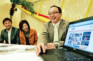 接客中に「花嫁テレビ」のサイト画面を見せる泉野民比古社長（右）＝名古屋市内のホテルで